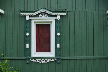 green wooden wall with a closed red door and a white-trimmed window, reflecting a classic and simple architectural style. sustainability and preservation of traditional architecture