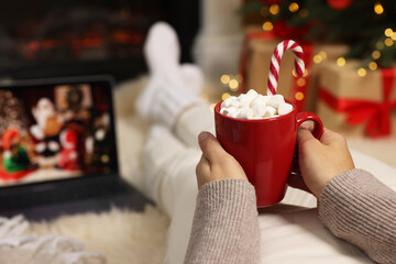 Woman drinking delicious cocoa and watching Christmas movie at home, closeup. Space for text