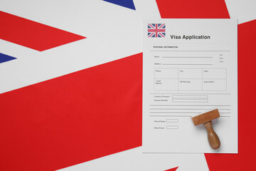 Immigration to United Kingdom. Visa application form and wooden stamp on flag, top view. Space for...