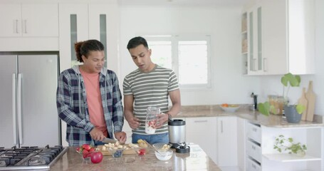 Happy diverse gay male couple preparing healthy fruit smoothie in kitchen, copy space, slow motion
