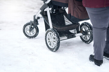 Naklejka premium Woman with baby carriage walk through snow sidewalk after heavy snowfall in the city. Woman push baby stroller, walking on snowy road in winter season.
