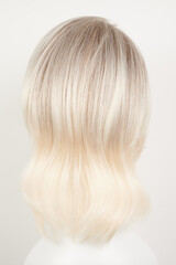 Naklejka premium Natural looking blonde fair wig on white mannequin head. Middle length hair cut on the plastic wig holder isolated on white background, back view