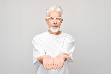 Gray-haired mature man 60 years old in white T-shirt holding something in hand, demonstrating empty...
