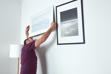 Man hanging pictures on the wall, cleaning and remodeling apartment. - obrazy, fototapety, plakaty