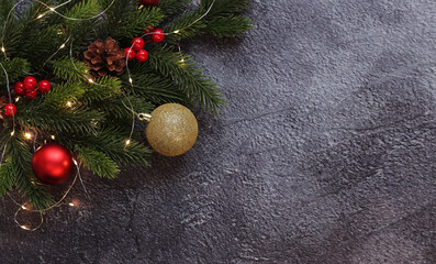 Fir branch with Christmas balls and glowing garland on a gray background, copy space. Place for text. Artificial spruce branch. Selective focus. New Year's composition