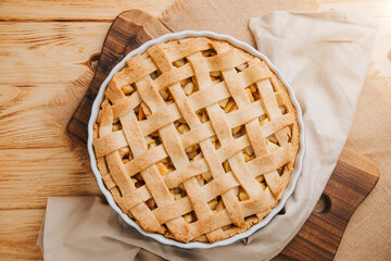 Apple pie in blue form on a light wooden background with a brown kitchen towel. Ready pie. Top view