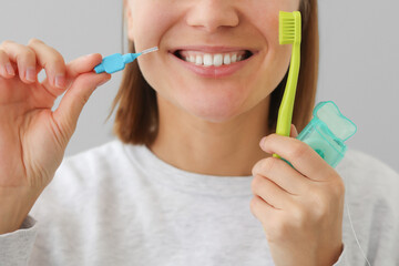 Unrecognisable woman with white teeth holds dental floss, toothbrush and interdental brush to for...