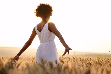 Young woman standing with arms outstretched in wheat field at sunset