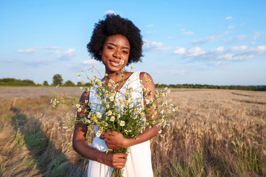 Happy young woman holding bouquet of daises in field