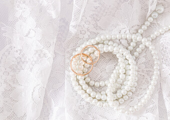 Two gold wedding rings lie on a luxurious vintage part of the bride's wedding dress with a string...