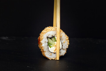Cheese sushi roll with sticks on a dark background.
