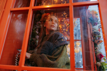 View through the glass to young woman dialing phone number in payphone booth.