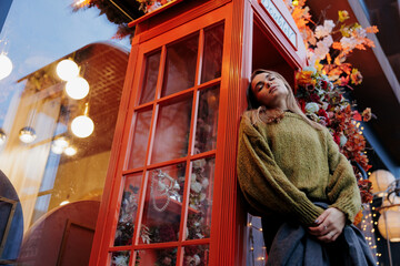 View to sad woman standing near retro telephone in payphone booth.
