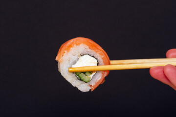 Sushi rolls are held on sticks on a dark background.