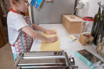 Little girl prepares homemade fresh pasta with a pasta machine in the kitchen. Preparing...