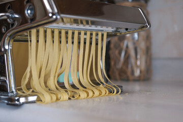 Cut Pasta in Domestic Kitchen,Fresh pasta and pasta machine on the kitchen counter while rolling...