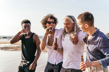 Happy multi-ethnic friends having beer and spending leisure time at beach