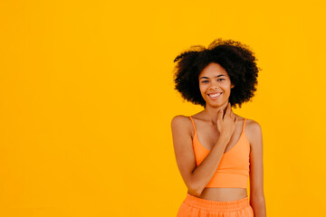 Smiling woman touching neck standing against yellow background