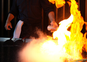 Chef cooking at stove with fire flame, close-up, selective focus