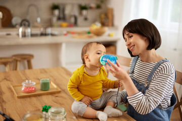 Mother giving her baby boy to drink water from baby bottle at home