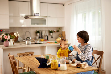 Mother giving her baby boy to drink water from baby bottle at home