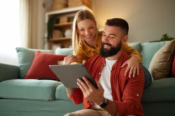 Fotobehang Handsome couple relaxing at home and looking at tablet © Stockphotodirectors