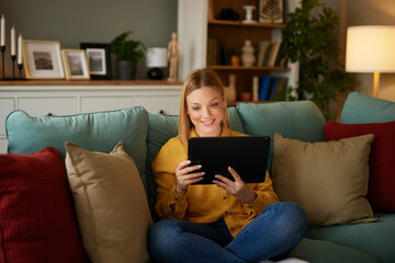 Relaxed woman sitting on sofa using digital tablet at home