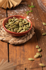Fototapeta na wymiar Bowl with pumpkin seeds on rustic wooden background, closeup. Healthy food concept