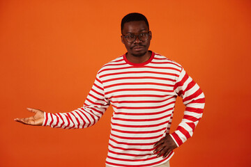 Young handsome black man with arm out in a welcoming gesture isolated on orange background
