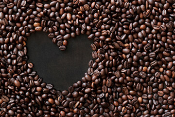 Coffee beans are laid out in the shape of a heart on a dark wooden surface. Top view. Roasted coffee beans, copy space