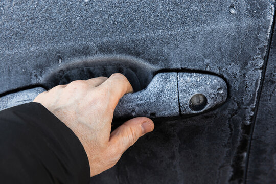 Hand trying to open locked door of a black car covered with frost