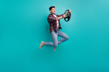 Full length photo of cheerful funky guy wear checkered shirt jumping high driving car isolated teal...