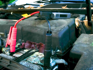 Dead corroded battery with alligator clips connects jump starter ready to start vehicle ignition, terminals electrical problems, under hood emergency roadside assistance, auto repair