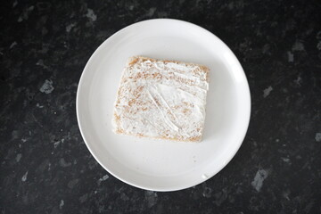 White cream cheese spreaded in a white toast at a black kitchen table. above view.