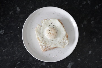 Close up of a fried eggs in a white plate at a black kitchen table.