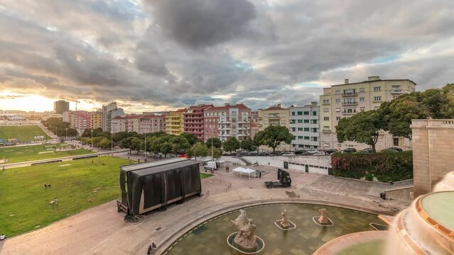 Panorama showing aerial view of Jardim da Alameda in Lisbon with the Luminous Fountain (Fonte Luminosa) timelapse during sunset. Dramatic clouds over colorful houses around square with green lawn