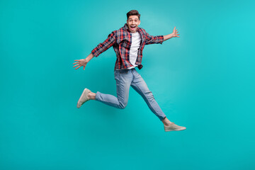 Full length photo of impressed cheerful guy wear checkered shirt jumping high having fun isolated...