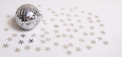 The disco ball lies on a white background strewn with silver snowflakes. New Year and Christmas...