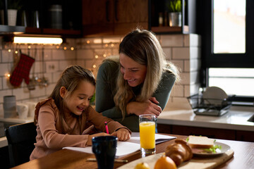 Morning joy in the kitchen: A smiling mother teaches her preschooler the art of writing letters at...