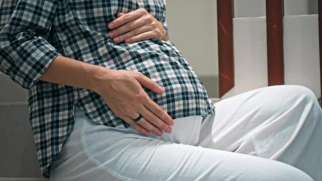 A young pregnant girl with a large stomach, stands at home on the stairs and touches her stomach with her hands.