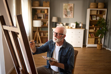 Elderly man painting on a canvas at home - Powered by Adobe