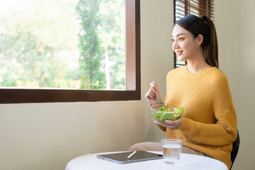 Smiling beautiful young woman likes to eat healthy fresh vegetable salad for breakfast. Dieting,...