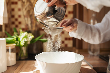 Woman sieving flour for dough. Baking bread at home, culinary at home, kitchen on the background