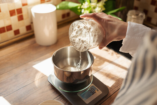 Woman making dough for a bread. Close up of hands of a girl adding some flour to dough, following recipe of baking bread