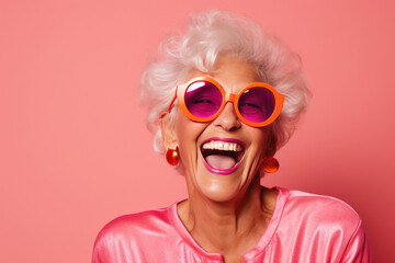 Happy senior woman in pink eyeglasses and hat on orange background