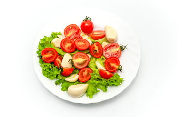 White plate of salad with vegetables on white background. Top view. Tomato, pepper, salad, garlic.