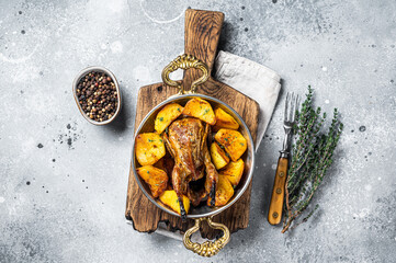 Oven baked quail with potatoes, spices and herbs in a skillet. Gray background. Top view