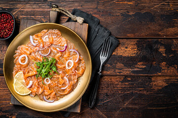 Italian Salmon carpaccio with onion and arugula served on a plate. Wooden background. Top view....