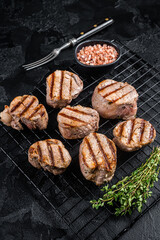 Grilled pork medallions steaks from tenderloin meat on a rack. Black background. Top view