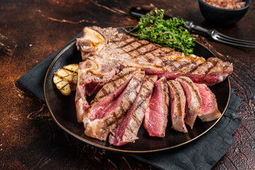 Grilled Medium rare Porterhouse, T-Bone Steak sliced in a plate. Dark background. Top view